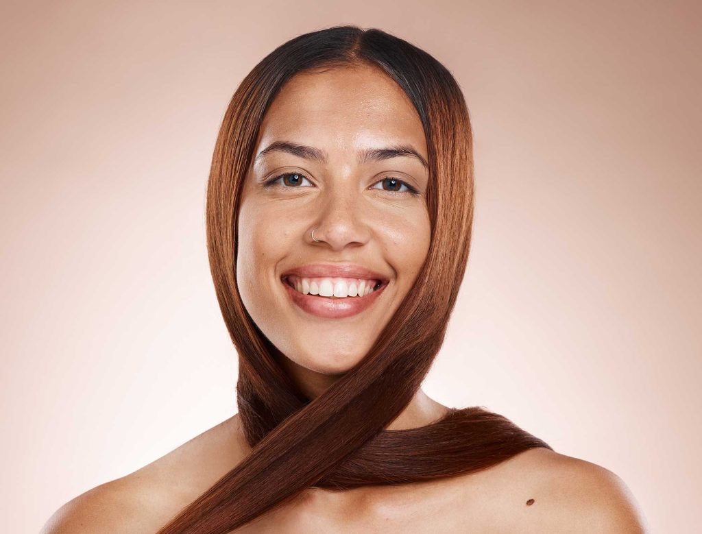 Smiling woman with straight brown hair encircling her neck, set against a soft beige background. She exudes warmth and confidence.